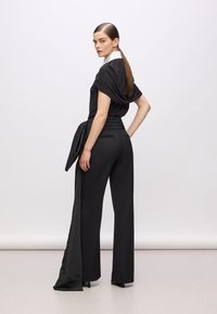 Schwarzes Outfit mit einem drapierten Oberteil mit weißem Kragen und hoch taillierten, weit geschnittenen Hosen. Glattes Material mit einem strukturierten Bund.