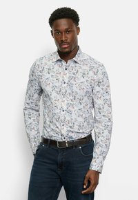 Weißes Hemd mit Knopfleiste und floralen Mustern in Pastellfarben. Lange Ärmel, strukturierten Kragen und kombiniert mit dunkelblauen Jeans.