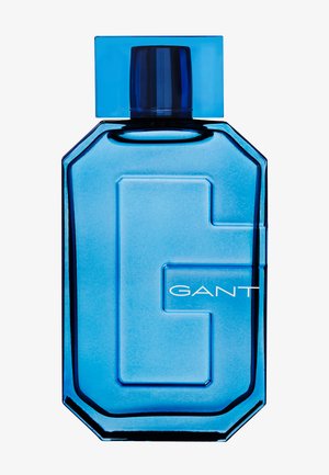 Blue glass perfume bottle with octagonal shape, transparent cap, and raised "G" logo. Features smooth texture and clean design.