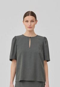 Dunkelgraue Bluse mit kurzen Ärmeln, Rundhalsausschnitt und einem kleinen Schlüsselloch, aus weichem, fließendem Stoff mit dezenten Puffärmeln.