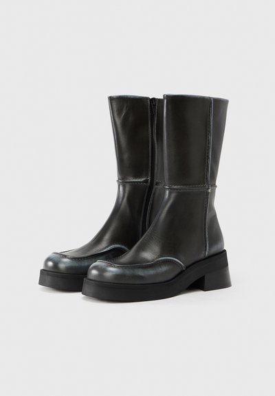 Μαύρα δερμάτινα μποτάκια μέχρι τον αστράγαλο με λεία υφή, στρογγυλερή μύτη, πλαϊνό φερμουάρ και χοντρό τακούνι. Διαθέτουν ραφές σε αντίθετο χρώμα και κομψό σχεδιασμό.