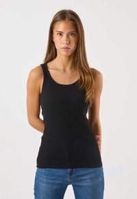 Zwart geribd tanktop met brede schouderbanden en een diepe ronde hals, gecombineerd met een blauwe spijkerbroek. Eenvoudig ontwerp en strakke pasvorm.