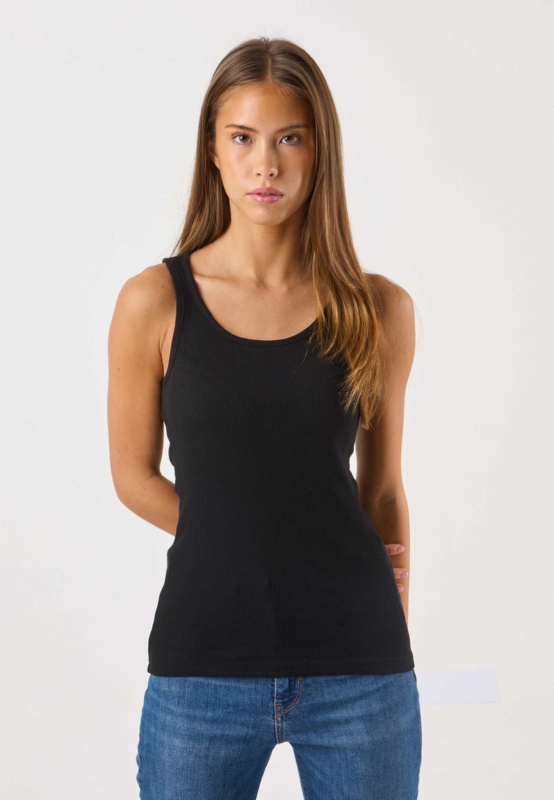 Zwart geribd tanktop met brede schouderbanden en een diepe ronde hals, gecombineerd met een blauwe spijkerbroek. Eenvoudig ontwerp en strakke pasvorm.