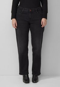 Jean en denim noir avec coupe droite, cinq poches, coutures discrètes et fermeture par bouton à la taille. Porté avec des bottines.