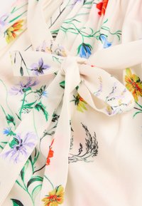 Lekko teksturowana tkanina z kwiatowym wzorem w odcieniach fioletu, czerwieni, żółci i zieleni. Z przodu znajduje się ozdobna kokarda.