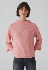 Top rosa texturizzato con scollatura ampia e maniche a tre quarti, con fessure laterali. Abbinato a pantaloni di denim scuro.