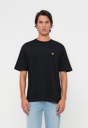 Black cotton t-shirt featuring a round neckline and short sleeves, with a small yellow eagle logo on the chest. Worn with light blue jeans.