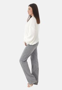 Suéter blanco, holgado, de punto con mangas largas combinado con jeans de tiro alto en un gris claro y sandalias beige.