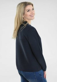 Marineblauwe pullover met textielbreisel, lange mouwen en een relaxte pasvorm, gecombineerd met donkerblauwe jeans. De achterkant toont de halslijn en de silhouet.