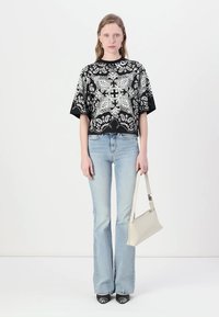 Svart og hvit mønstret oversized t-skjorte, lyseblå vid jeans, kort hvit håndveske, og svarte spisse sko.