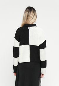 Sweater curto em malha com um padrão em bloco preto e branco, com textura canelada e colarinho. Inclui uma etiqueta na parte de trás.