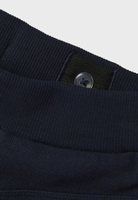 Tejido acanalado azul marino con una textura suave, que cuenta con un botón y una banda elástica para un ajuste ajustable en la cintura.