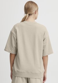 Beige oversized sweatshirt med korta, lösa ärmar och ribbad rund halsringning. Mjuk textur och minimala sömmar, designad för komfort.