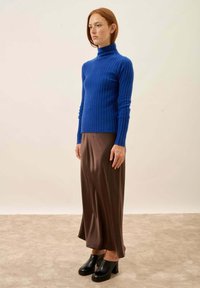 Blå ribbad polotröja, tillsammans med en brun satin midikjol. Svarta klackskydd slutför outfiten. Slät textur, smal passform.