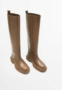 Een paar hoge, bruine leren laarzen met dikke profielzolen en trekriempjes aan de achterkant, rechtop staand op een witte ondergrond.