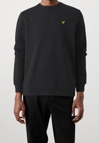 Zwarte sweatshirt van katoen met lange mouwen, geribbelde boorden en zoom, met een klein geel arendlogo op de linkerkant van de borst.