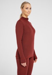 Long-sleeve top in dark red fabric with a zip neck, slim fit, and thumbhole cuffs, paired with matching fitted pants. Smooth texture.