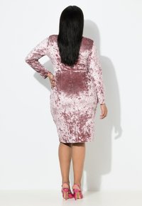 Robe midi en velours rose avec manches longues et silhouette ajustée. Texture remarquable avec brillance. Assortie à des talons rose à lanières.