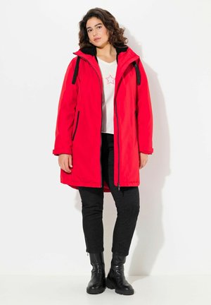 Red parka jacket with a fur-lined hood, zippered front, side pockets, and black accents. Worn over a white shirt and black pants. Black boots visible.