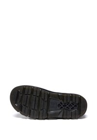 Semelle de botte noire avec des crampons profonds, des zones de prise texturées, et un logo en forme de croix sur un fond blanc éclatant.