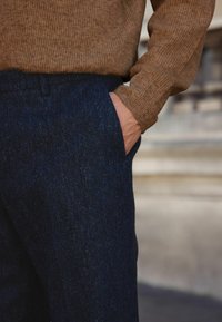 Marineblauwe wollen broek met een subtiele textuur, voorzien van zijzakken. Gecombineerd met een bruine geribbelde gebreide trui met een comfortabele pasvorm.