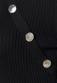 Černá žebrovaná tkanina má diagonální popruh se třemi lesklými stříbrnými knoflíky s vyrytým textem. Textura je zřetelně vyvýšená.