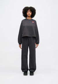 Σκούρος γκρι κοντός φούτερ με μακριά μανίκια, διαθέτει ένα μικρό κόκκινο λογότυπο. Συνδυάζεται με άνετους σκούρους γκρι φούτερ παντελόνες και μαύρα αθλητικά παπούτσια.