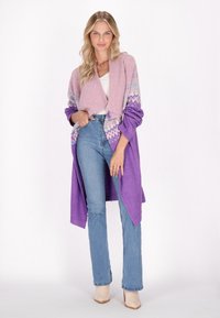 Lila och rosa stickad cardigan med ett geometriskt mönster, öppen framtill, lång ärm, bärs över blå utsvängda jeans och beige klackboots.