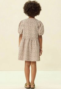 Kleid mit Leopardenmuster, gepufften Ärmeln, tailliertem Schnitt und ausgestelltem Rock. Beiger Stoff mit braunen Flecken. Sandalen mit Schnallen-Detail.