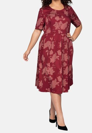 Robe fleurie bordeaux avec manches courtes, jupe évasée et tissu fluide. Présente un col rond et de grands motifs de fleurs roses.