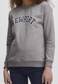 Felpa grigia con la scritta "NEWPORT" in blu che si incurva sulla parte anteriore. Presenta polsini e orlo a costine, realizzata in un materiale morbido e texturizzato.