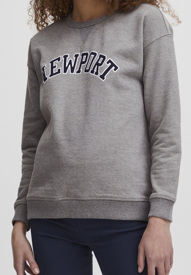 Felpa grigia con la scritta "NEWPORT" in blu che si incurva sulla parte anteriore. Presenta polsini e orlo a costine, realizzata in un materiale morbido e texturizzato.