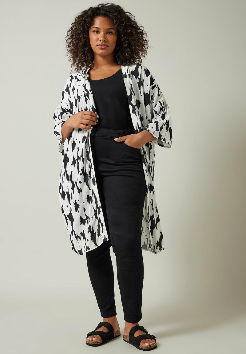 Lekki kimono w czarno-białą kratkę houndstooth, w połączeniu z czarną bluzką i spodniami; sandały z korkową podeszwą i paskami.