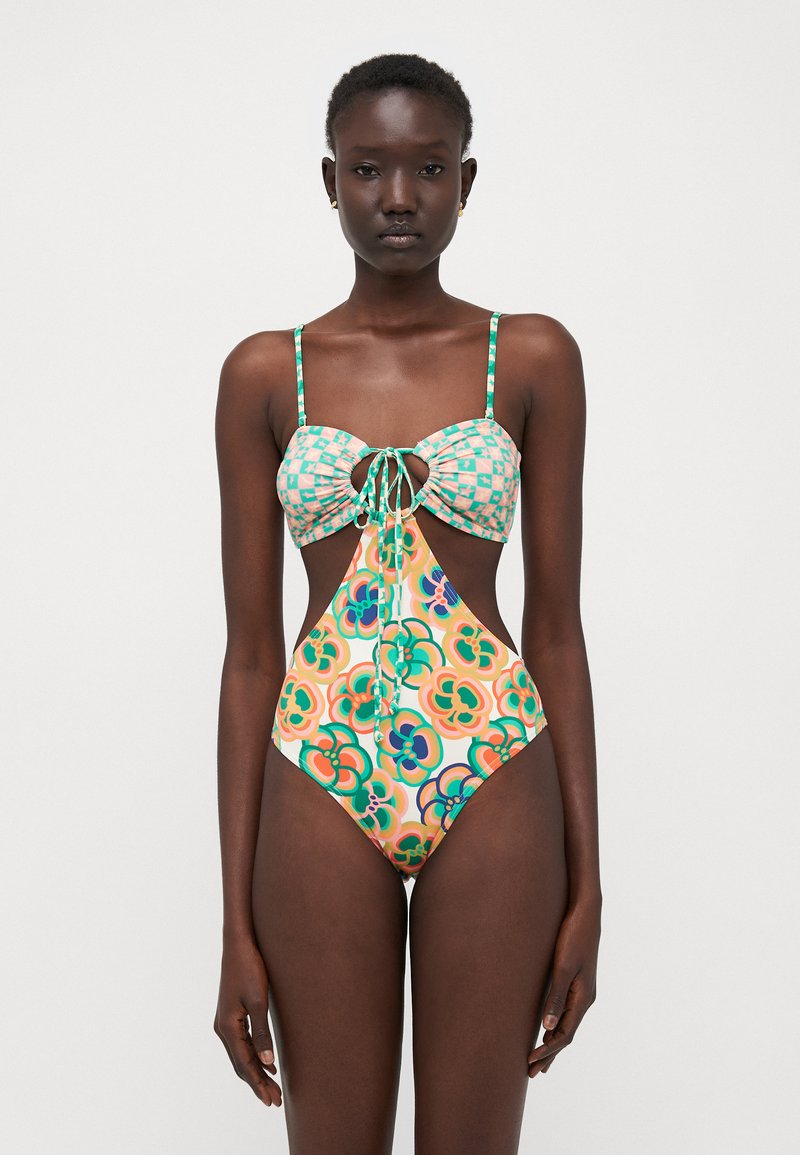Maillot de bain multicolore avec un haut à motifs présentant un lien central, des côtés découpés et un bas uni. Le matériau semble lisse et extensible.