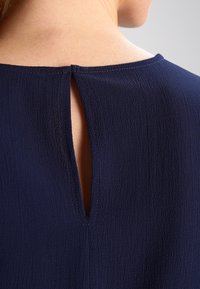 Blusa blu navy in tessuto texture, con scollatura rotonda e apertura a chiave sul retro. Cuciture ordinate lungo i bordi.