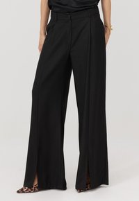 Czarne spodnie o szerokich nogawkach i wysokim stanie, z bocznymi rozcięciami i gładkim materiałem. Do tego szpilki w panterkę.