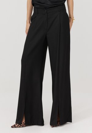 Czarne spodnie o szerokich nogawkach i wysokim stanie, z bocznymi rozcięciami i gładkim materiałem. Do tego szpilki w panterkę.