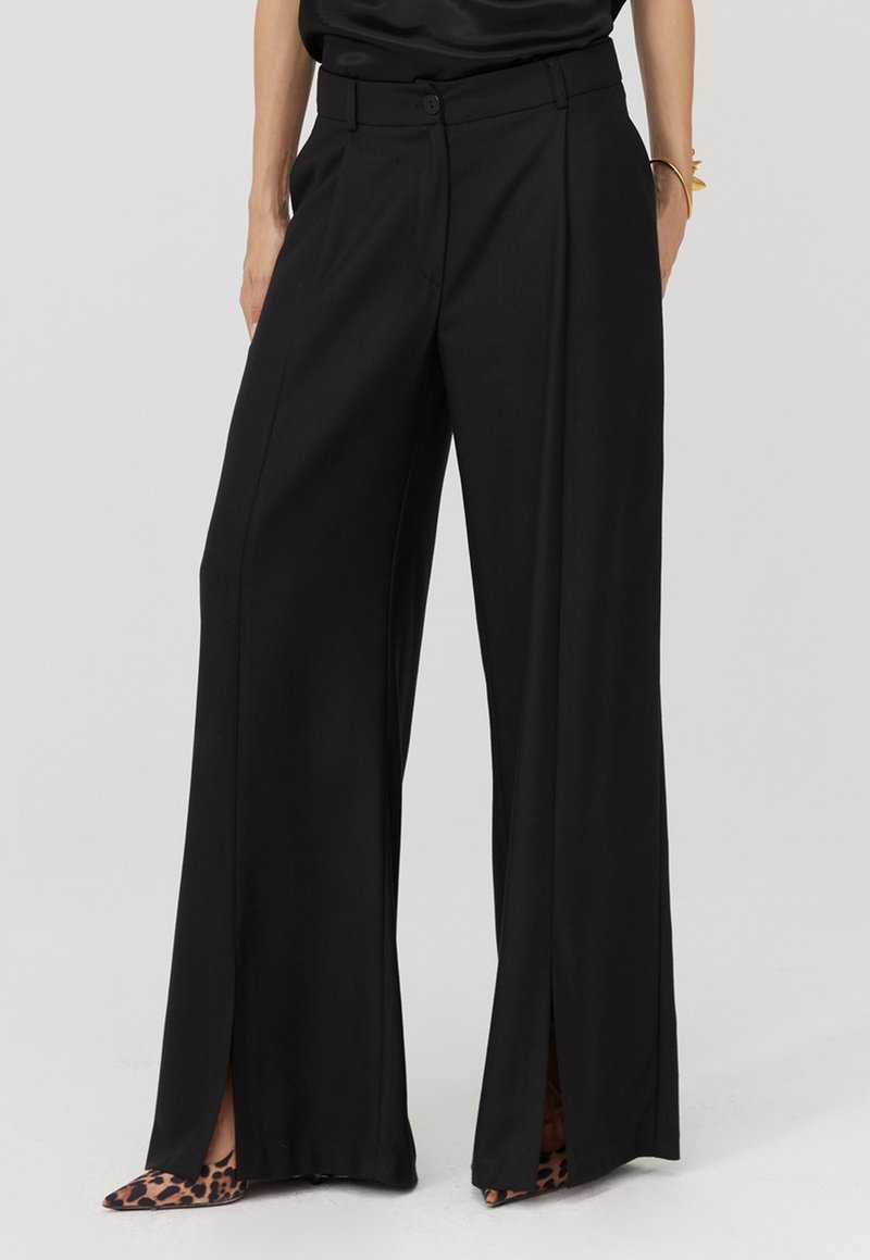 Czarne spodnie o szerokich nogawkach i wysokim stanie, z bocznymi rozcięciami i gładkim materiałem. Do tego szpilki w panterkę.