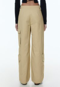 Beige cargobroeken met een losse pasvorm, voorzien van zijzakken en een gladde afwerking. De tailleband is plat met minimale details.