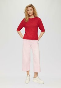 Roter gestrickter Pullover mit kurzen Ärmeln, kombiniert mit hellrosa weit geschnittenen Hosen und weißen Plateausneakern. Einfaches, lässiges Outfit.