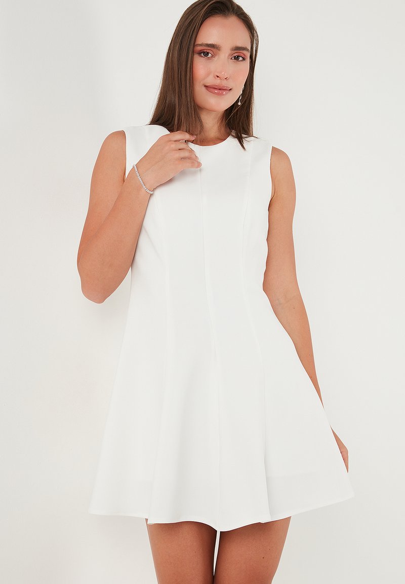 Witte mouwloze jurk met een uitlopende silhouette, gekenmerkt door een gladde textuur en subtiele naaddetails, met een lengte tot halverwege de bovenbenen.