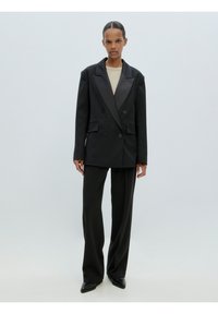Dubbelzijdig zwarte blazer met satijnen revers, gecombineerd met loszittende zwarte broek. Gladde stof en scherpe silhouet.