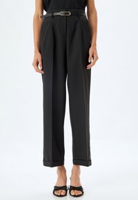 Pantaloni neri a vita alta con pieghe, cintura con fibbia dorata e orlo corto, realizzati in tessuto leggero e morbido.