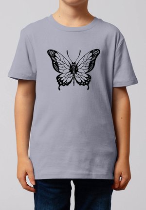 Kind trägt ein hellgraues T-Shirt mit einem detaillierten schwarzen Schmetterlingsmotiv auf der Brust, kombiniert mit dunkelblauer Hose.