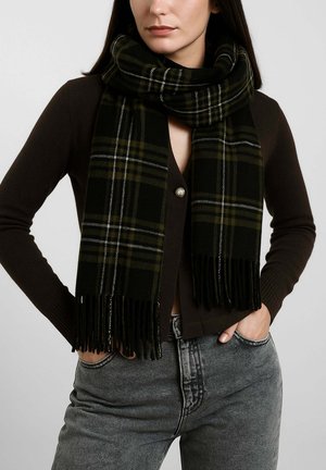 Sciarpa a quadri neri e verdi con bordi sfrangiati, realizzata in materiale morbido. Indossata in modo sciolto intorno al collo, abbinata a un cardigan scuro.