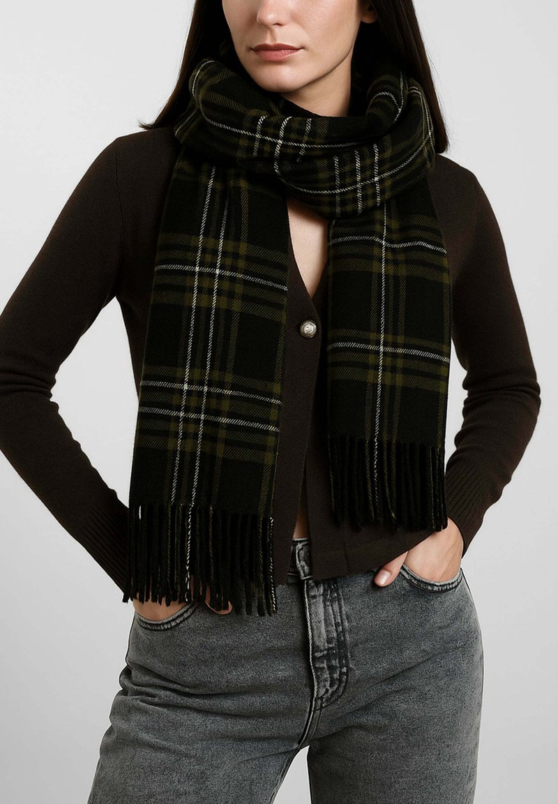 Sciarpa a quadri neri e verdi con bordi sfrangiati, realizzata in materiale morbido. Indossata in modo sciolto intorno al collo, abbinata a un cardigan scuro.
