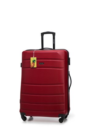 Valise rigide rouge avec une surface texturée, une poignée rétractable et quatre roues. Comprend une étiquette de bagage sur le thème de l'ananas.