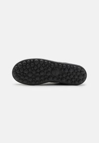 Suola di scarpa in gomma nera con superficie texturizzata e motivi circolari per una maggiore aderenza, realizzata per durabilità e comfort.