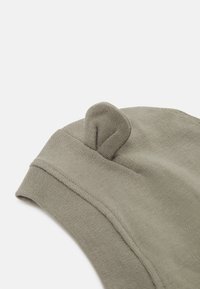 Cappello in cotone khaki con una texture morbida e un dettaglio a anello sulla sommità. Presenta un bordo arrotolato per un design casual.