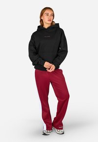 Čierna mikina s kapucňou a predným vreckom, červený nápis "PEGADOR"; v kombinácii s burgundskými teplákmi so bielymi bočnými prúžkami.